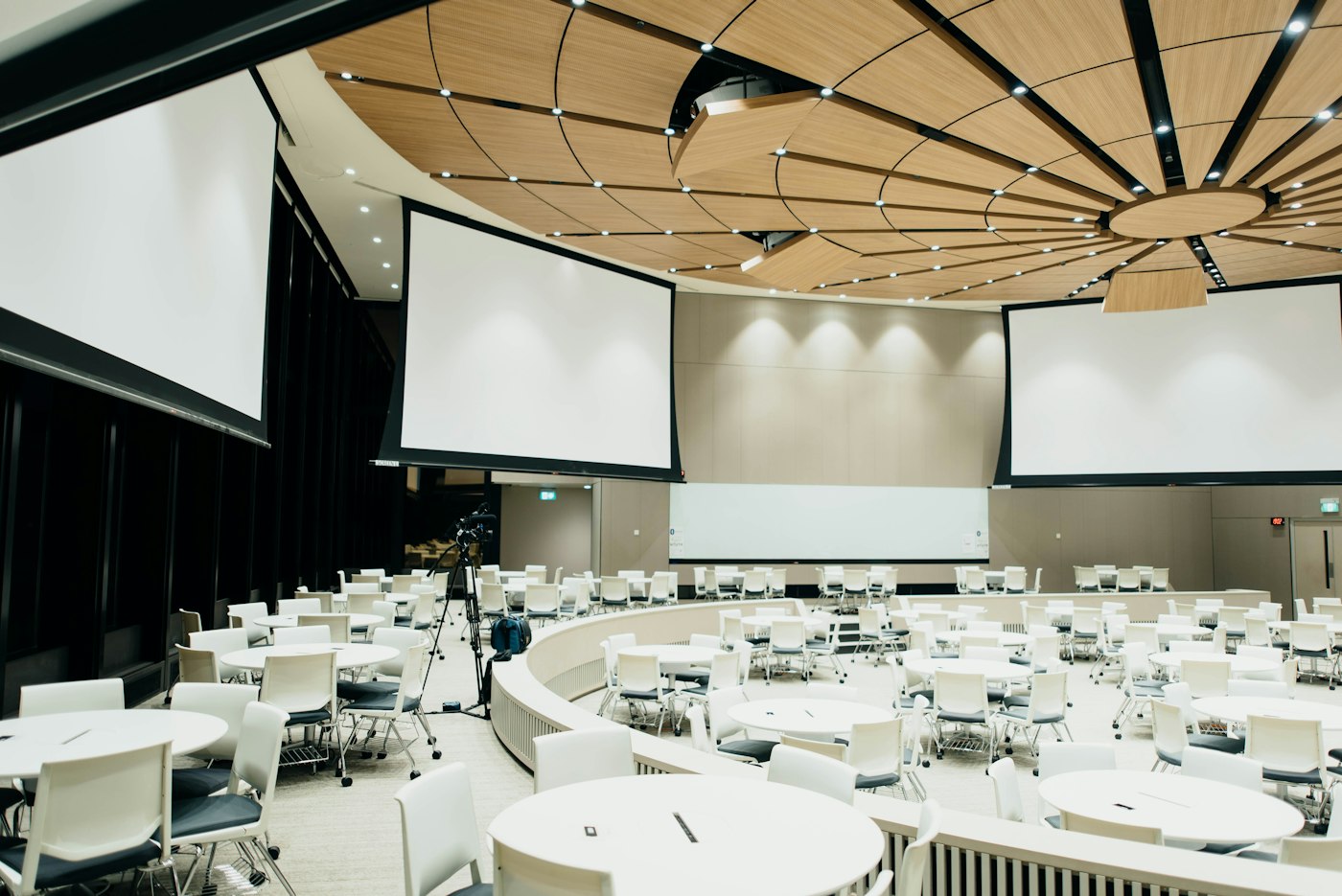 A large meeting room with round white tables and chairs set out before people arrive