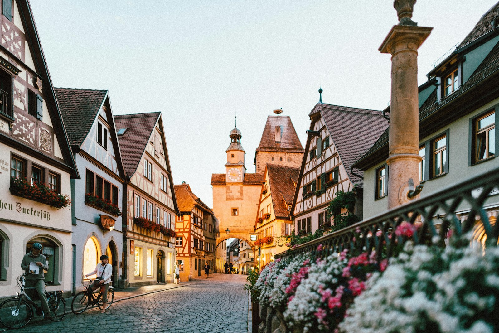 A cobbled street of timber-framed houses with flower boxes, leading to a clock tower over the lane